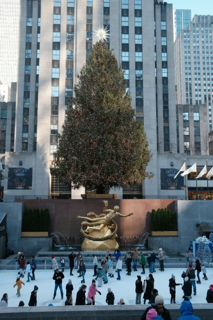 Christmas tree at Rockefeller Center with the rink and people skating, with the building behind it.