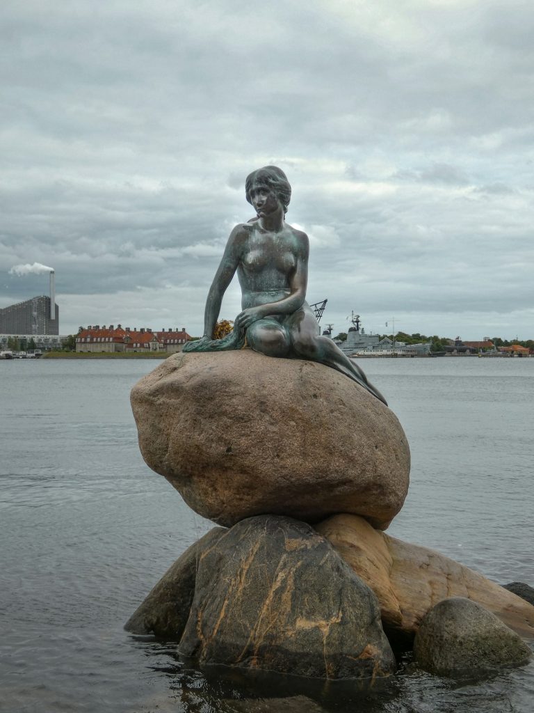 Estatua de la Sirenita sentada en una roca junto al agua en el puerto de Copenhague