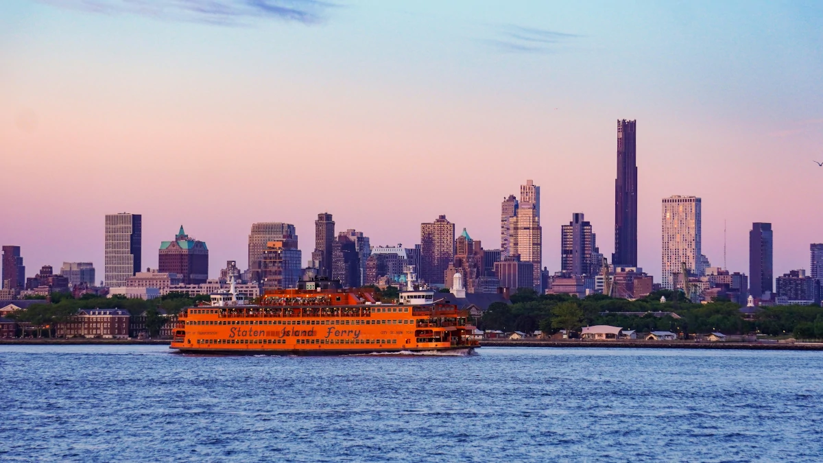 Staten Island Ferry crossing the waters with the Manhattan skyline in the background at sunset.
