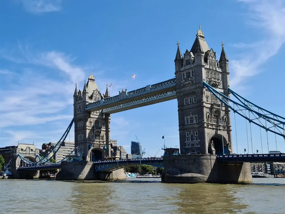 Tower Bridge seen from the River Thames in London, with its two Gothic towers and blue cables under a clear sky
